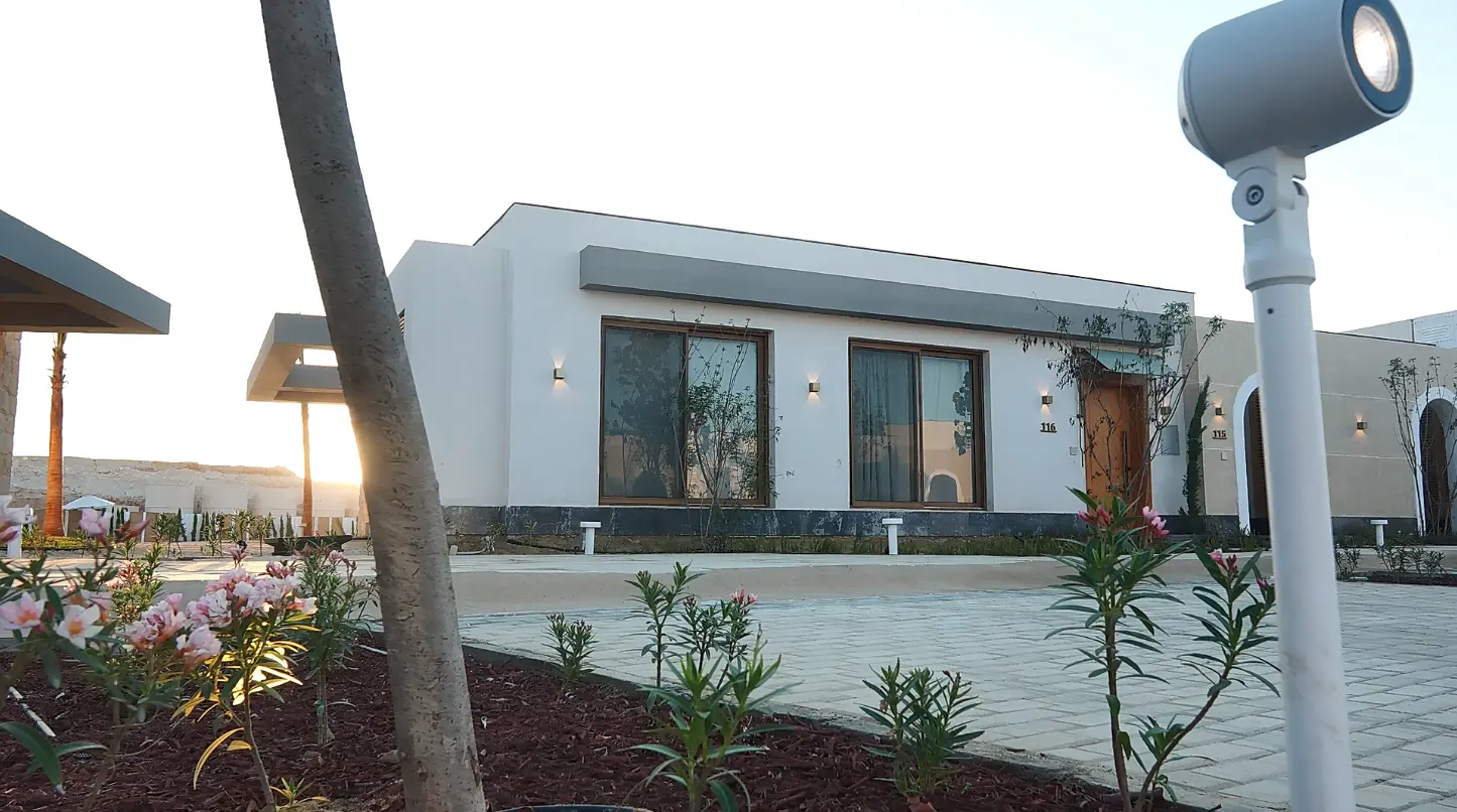 Exterior view of a finished chalet at The Med, featuring clean white architecture, wooden doors,landscaped gardens, and outdoor lighting